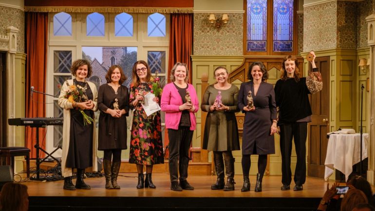 Gruppenfoto von 7 Frauen auf der Bühne mit Auszeichnungen und Blumensträußen.