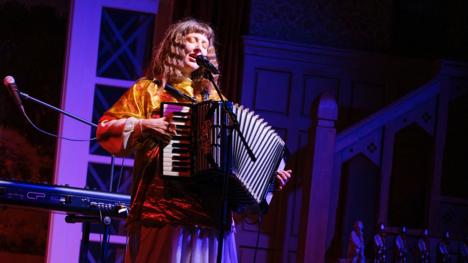 Sängerin mit Akkordeon auf einer lila beleuchteten Bühne