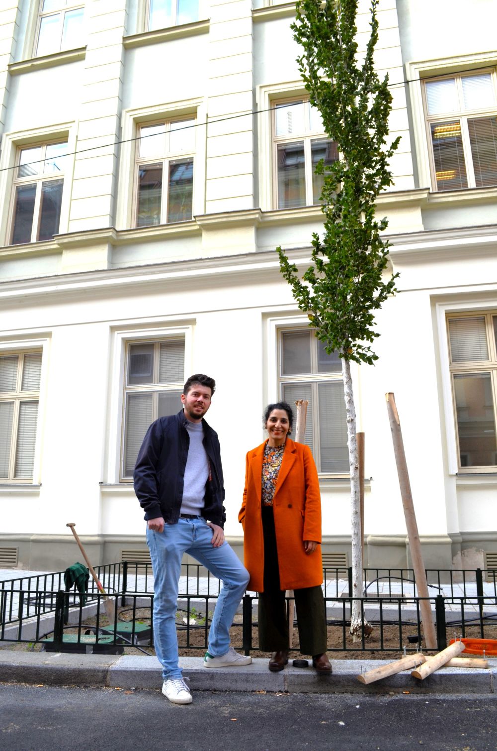 Ein Mann und eine Frau unter einem jungen, neu gepflanzten Baum im Stadtgebiet
