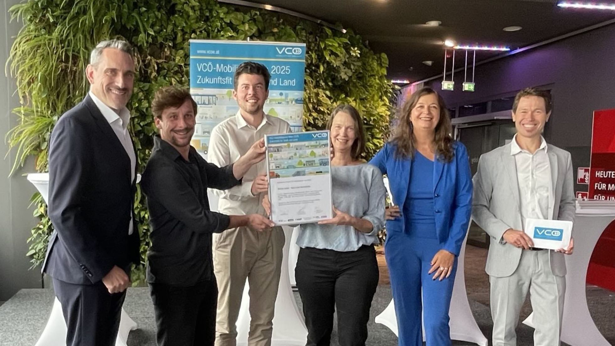 3 Männer und 3 Frauen blicken lächelnd in die Kamera. Der Mann und die Frau in der Mitte halten gemeinsam eine Urkunde hoch.