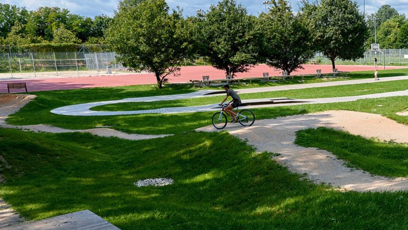 Ein Fahrradfahrer auf einem kurvigen Lehm-Radweg zwischen grünen Rasenflächen