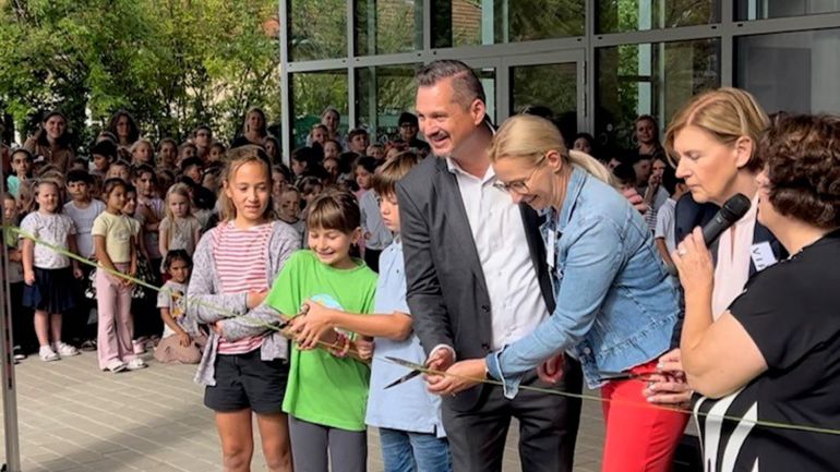 copyright: Vincent Bellemann 3 Kinder und 2 Erwachsene durchschneiden gemeinsam ein Band, im Hintergrund eine große Gruppe Schulkinder