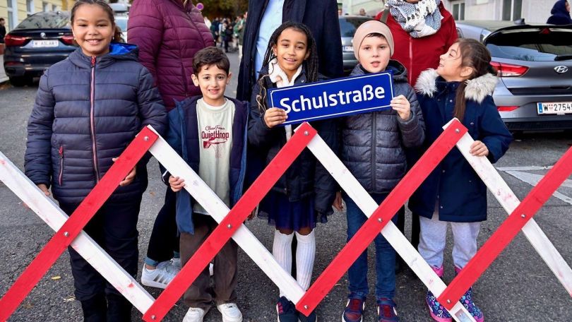 Kinder vor Absperrung mit Straßenschild "Schulstraßen".