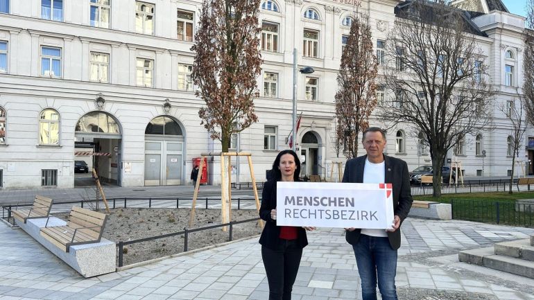 2 Personen mit Schild "Menschenrechtsbezirk" vor historischem Gebäude mit Vorplatz