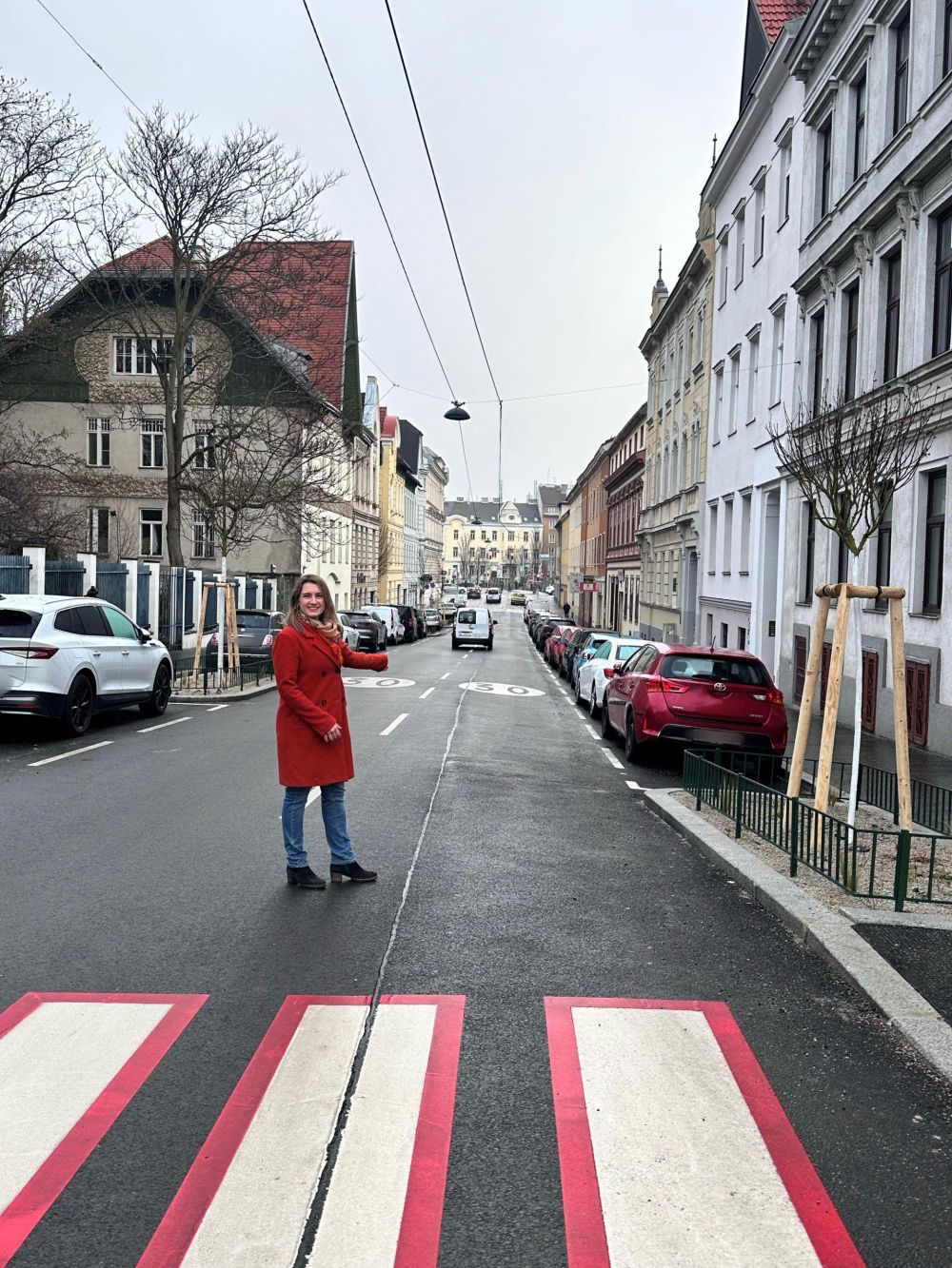 Frau im roten Mantel auf einer neu asphaltierten Straße mit Tempo-Bodenmarkierung "30".