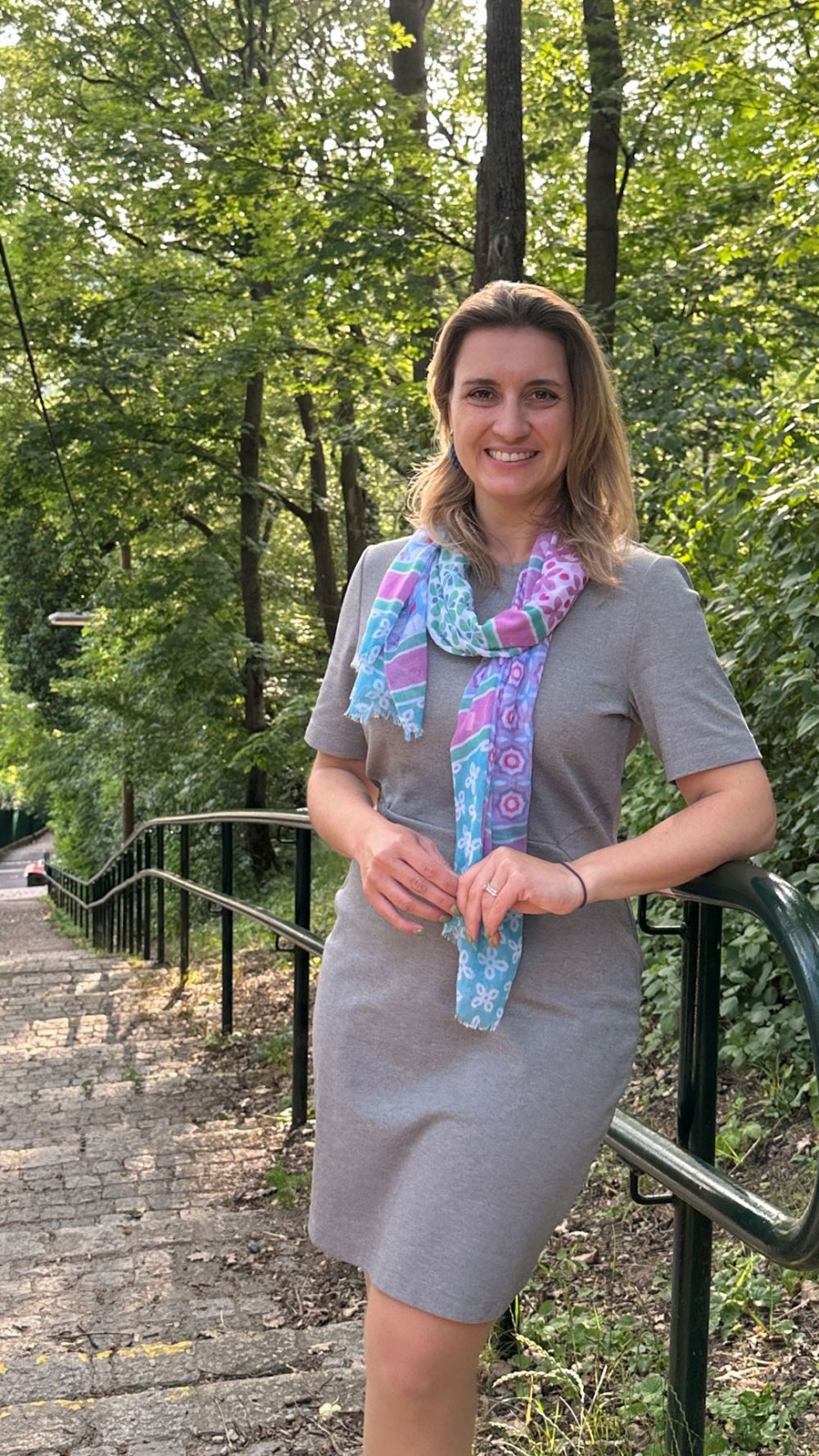Bezirksvorsteherin Johanna Zinkl trägt ein Sommerkleid; sie lehnt am Geländer des Steigs, hinter ihr sieht man die Treppen, die bergab führen