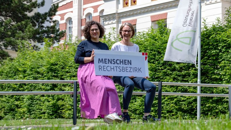 copyright: frischesgras - kommunikation & visuelles design 2 Frauen im Grünen halten ein Schild mit der Aufschrift "Menschenrechtsbezirks"