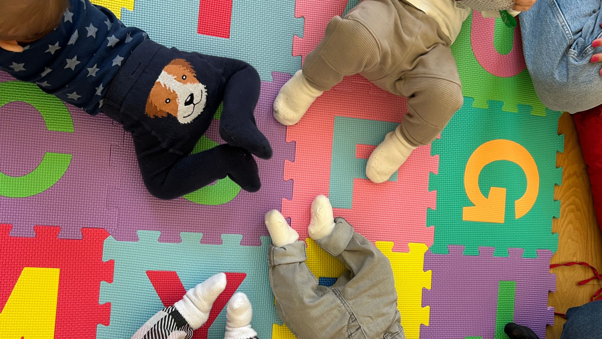 Einige Babys krabbeln oder liegen auf einer bunten Spielmatte am Boden.