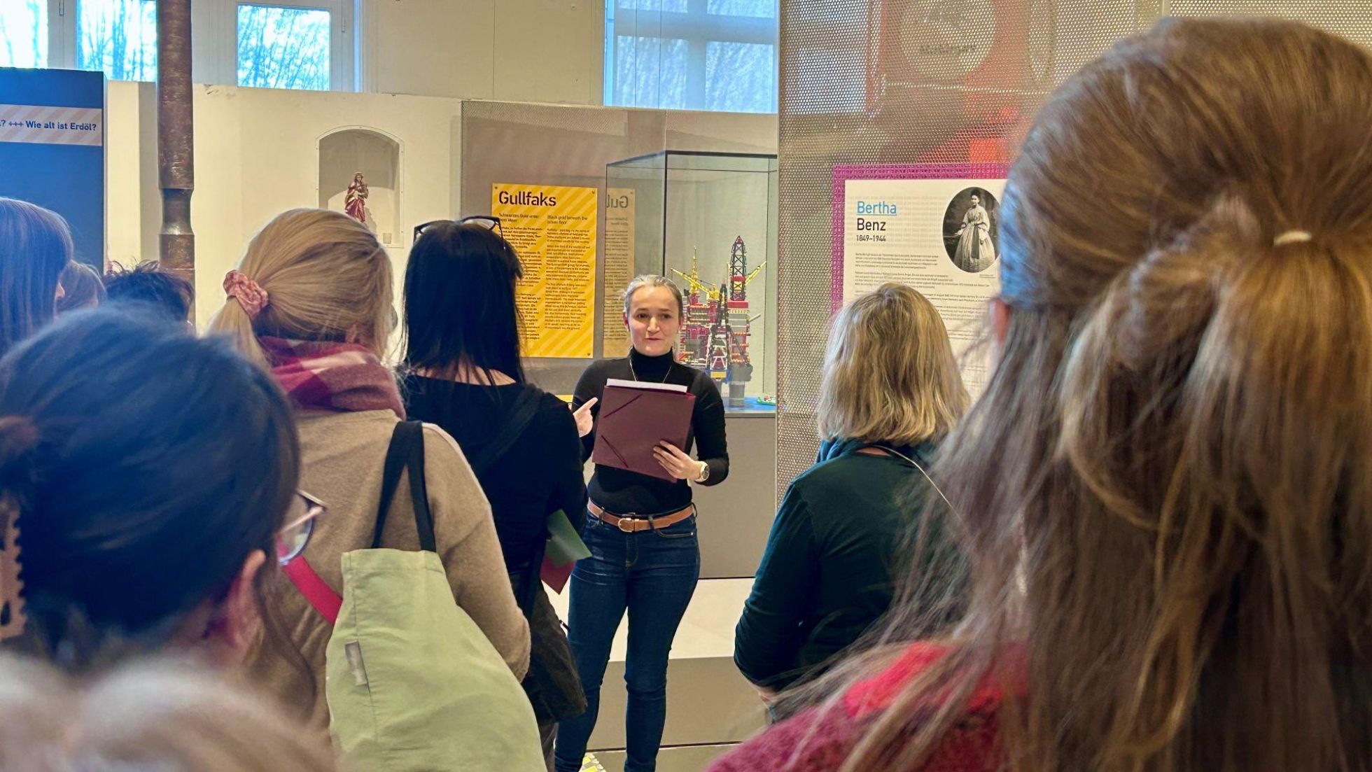 Eine Frau mit Mappe in der Hand führt andere Frauen durch eine Ausstellung