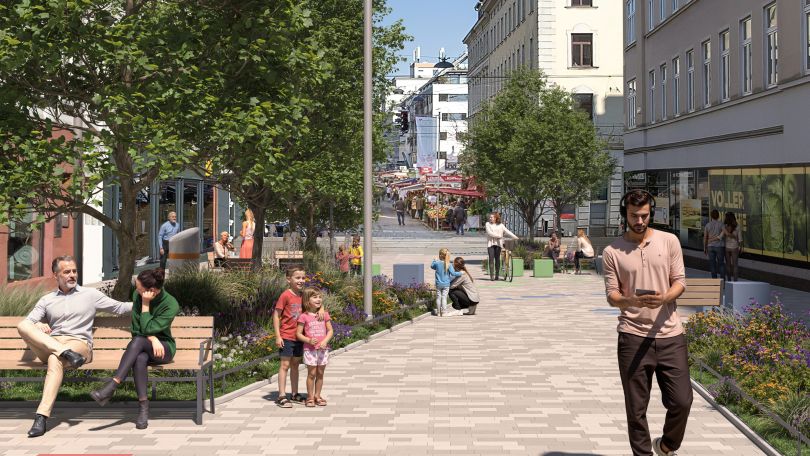 Fußgängerzone mit hellen Pflastersteinen, Gräser- und Blumenbeeten und 3 Bäumen. Verschiedene Menschen unterschiedlichen Alters gehen durch die Fußgängerzone und 2 Personen sitzen auf einer Parkbank.