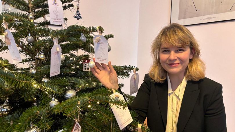 copyright: BV 16 Eine Frau steht neben einem Christbaum, auf dem neben Kugeln auch verschiedene Wunschzettel hängen.