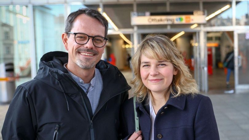 Ein Mann mit schwarzer Brille und schwarzer Jacke und eine Frau mit schulterlangen hellbraunen Haaren und schwarzer Jacke vor U-Bahn-Eingang "Ottakring".