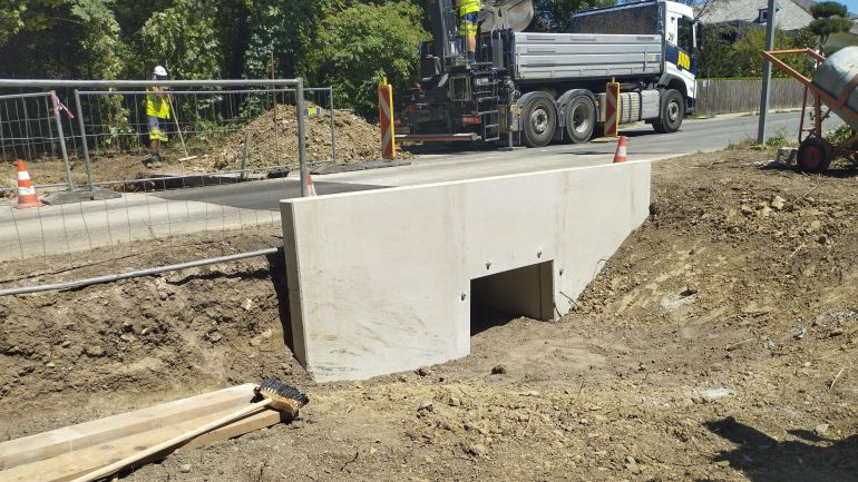 copyright: VGT.at Ein kleiner Tunnel führt unter einer schmalen Straße durch. Rund um die Straße ist eine Baustelle mit Absperrungen, Leitbaken, Lkw und Bauarbeitern.