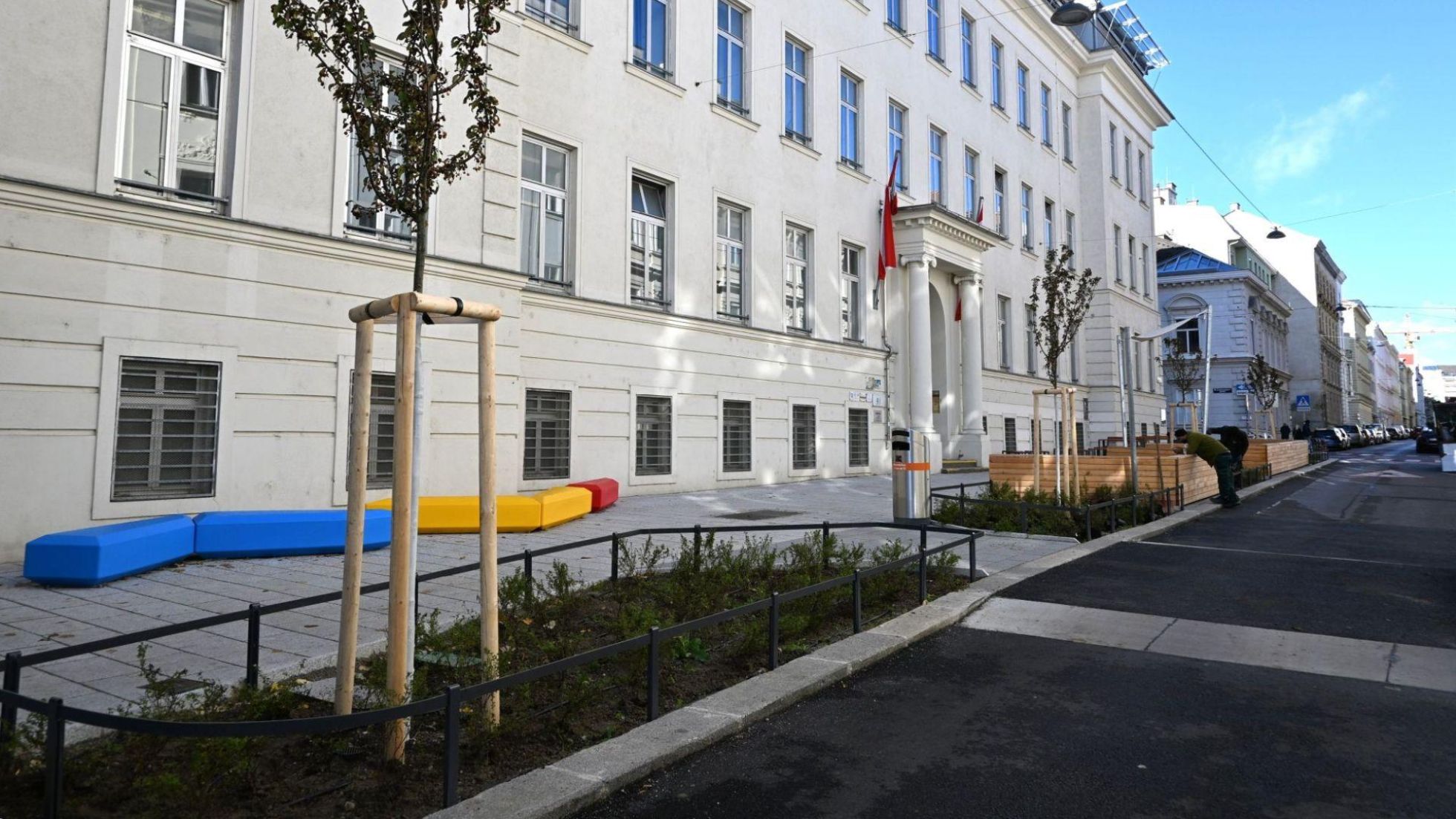 Neuer Schulvorplatz mit bunten Sitzmöbeln, Beeten und Bäumen.