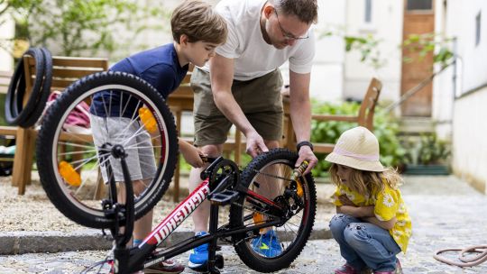 Ein Mann repariert mit 2 Kindern ein Fahrrad