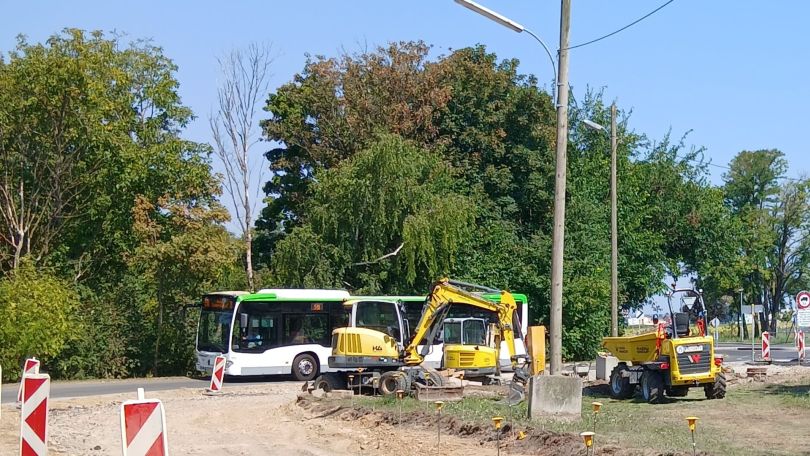 Ein Bus, zwei Bagger und ein Kipplaster neben einer Straße und Bäumen