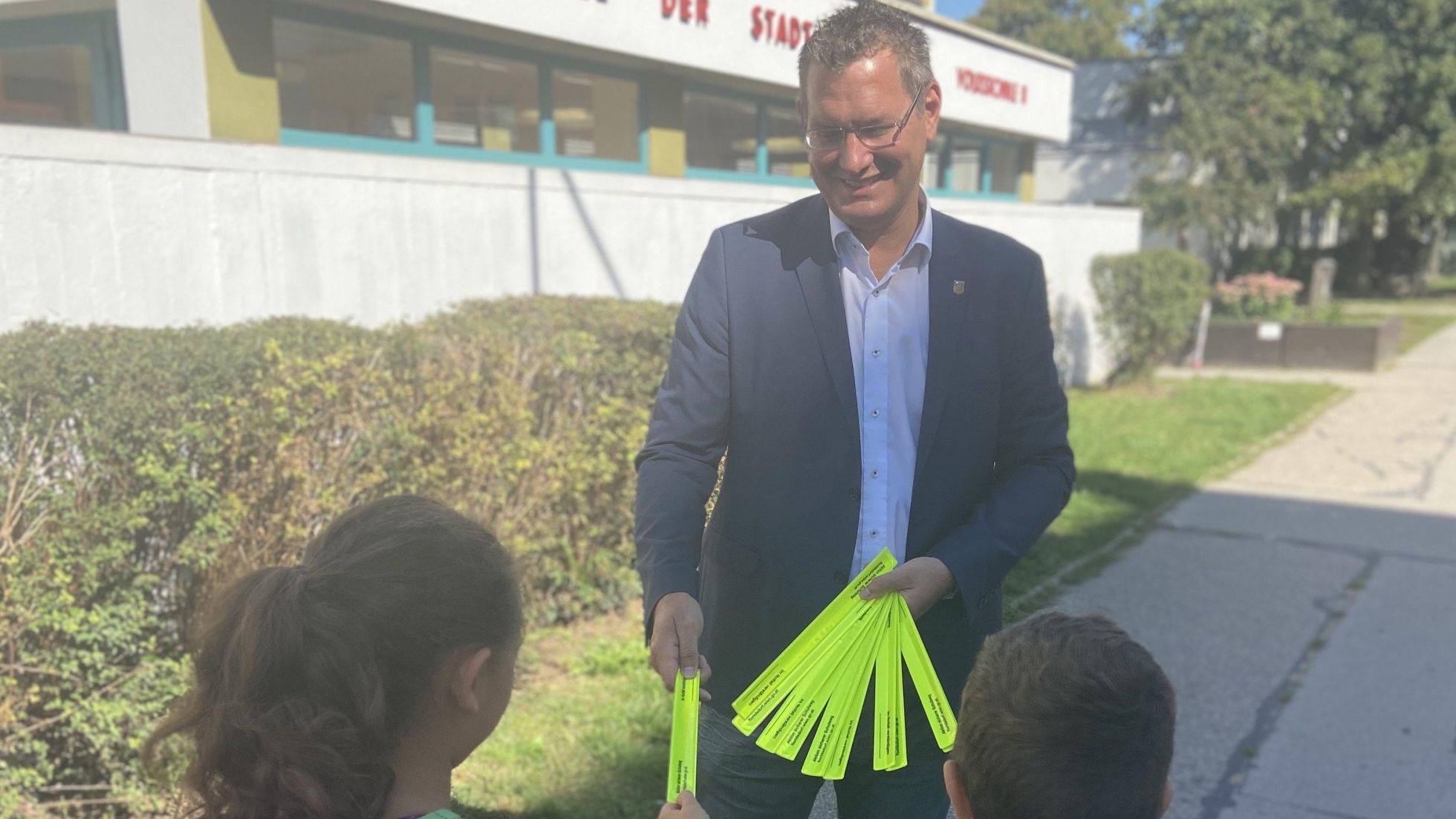 Bezirksvorsteher Georg Papai verteilt Refektor-Armbänder an 2 Kinder