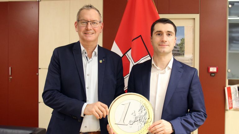 copyright: BV 21 2 Politiker halten eine große Euro-Münze.