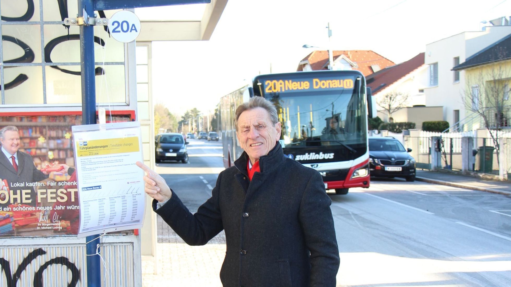 copyright: BV 21 Mann in schwarzem Mantel zeigt auf den Fahrplanaushang bei der Bushaltestelle, im Hintergrund ein Linienbus.