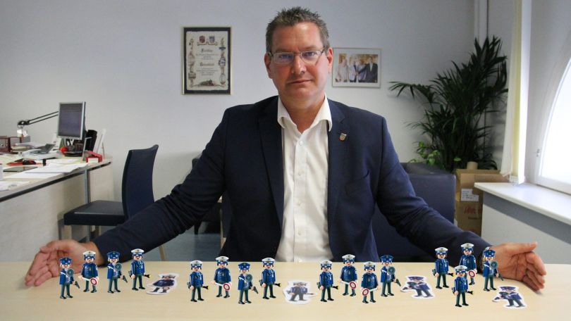 Bezirksvorsteher Papai streckt die Arme auf dem Tisch aus und auf dem Tisch stehen eingefügte Polizist*innen-Spielfiguren