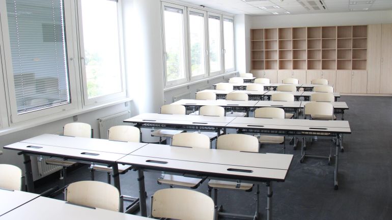 copyright: BV 21 Klassenzimmer mit mehreren Tischreihen in beige. Am Ende des Raumes steht ein großes Regal.