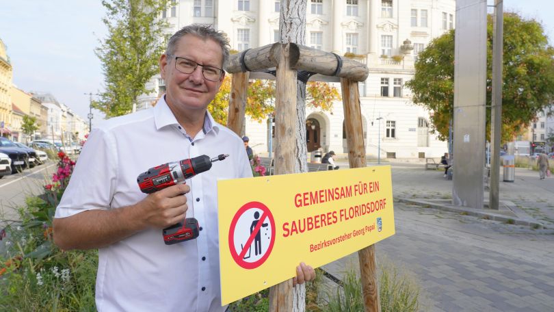 copyright: BV 21 Ein Mann mit einem Bohrer in der rechten Hand und einem Schild mit der Aufschrift "Gemeinsam für ein sauberes Floridsdorf" in der linken Hand.
