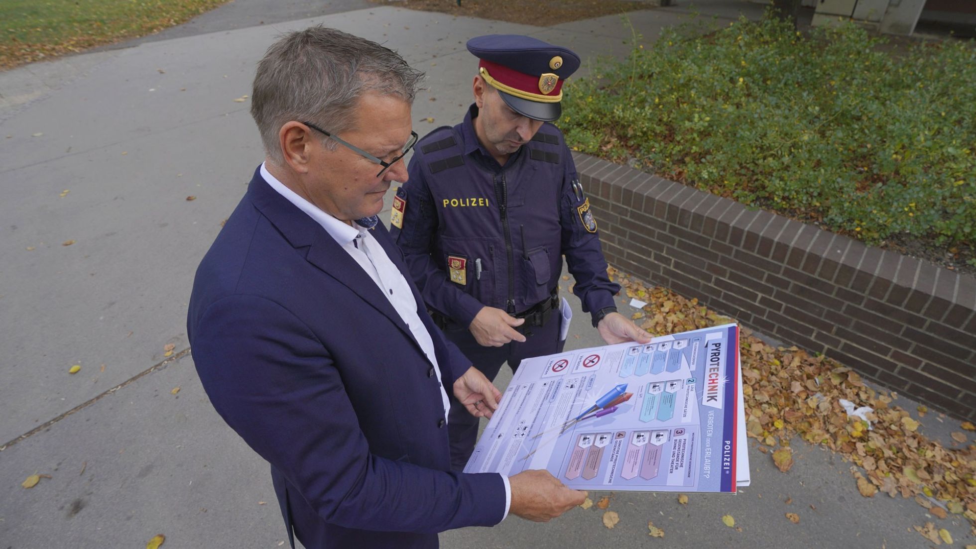 copyright: BV 21 Bezirksvorsteher Georg Papai steht neben einem Polizisten. Sie betrachten ein Plakat zum Böllerverbot.