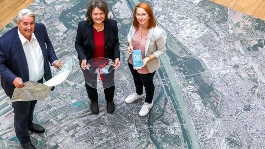 BV Nevrivy und 2 Frauen stehen auf einem überdimensionalen Wien-Plan