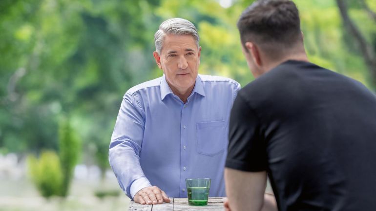 Ernst Nevrivy im Gespräch mit einem Mann; sie sitzen in einem Park an einem Tisch