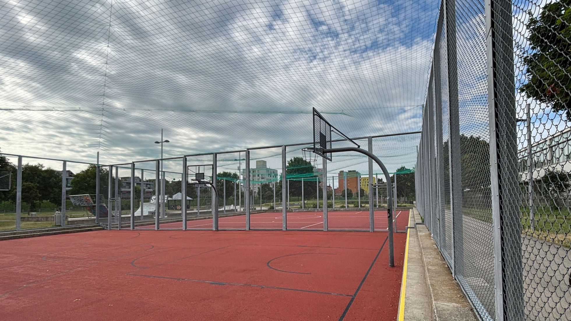 Sportplatz mit Basketballkorb, modernem roten Bodenbelag und und Umzäunung