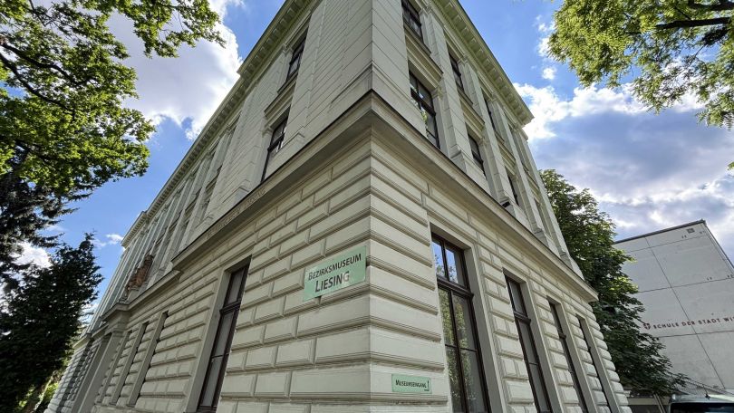 Fassade des Liesinger Bezirksmuseums, an der cremefarbenen Wand des Altbaus hängt ein Hinweisschild "Bezirksmuseum Liesing".