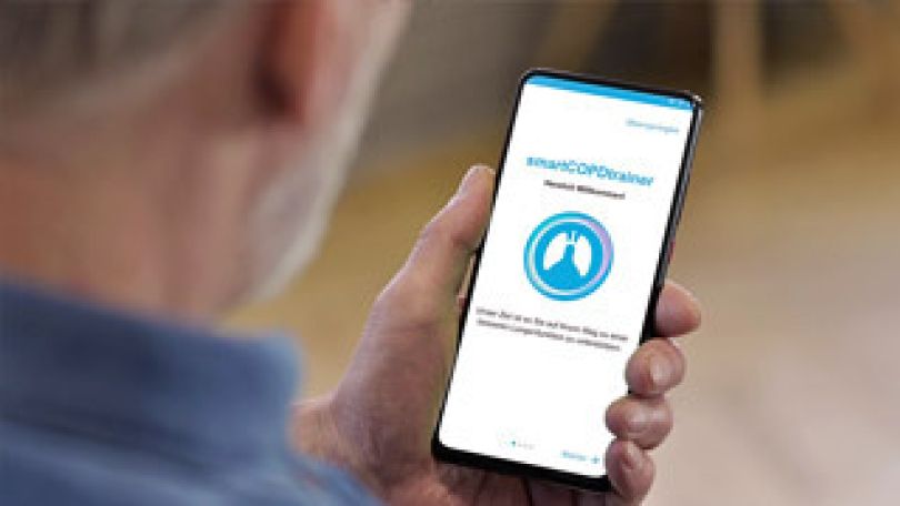 Ein älterer Mann hält ein Handy in der Hand und ruft die COPD App auf
