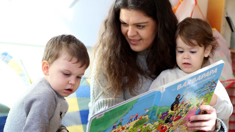 copyright: MA 10 - Wiener Kindergärten/VOTAVA Frau liest 2 Kindern etwas aus einem Buch vor.
