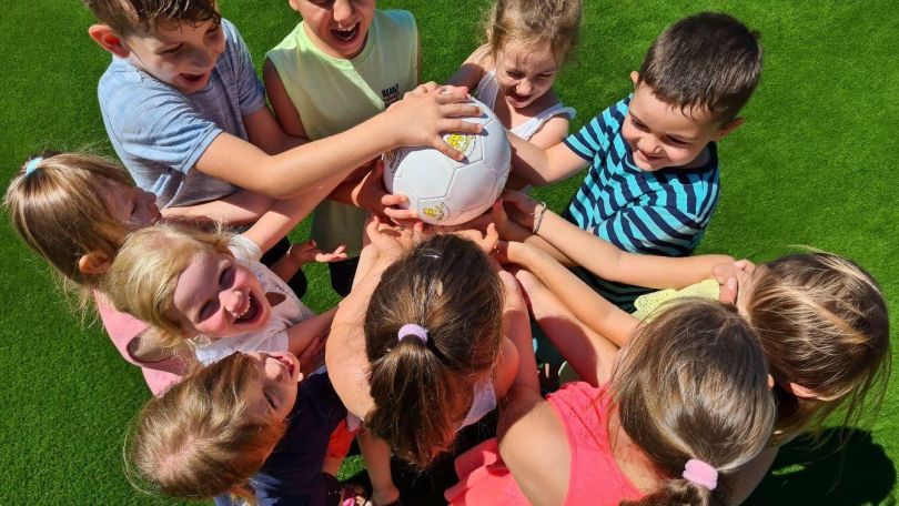 Mehrere Kinder stehen in einem Kreis und legen ihre Hände auf einen Ball