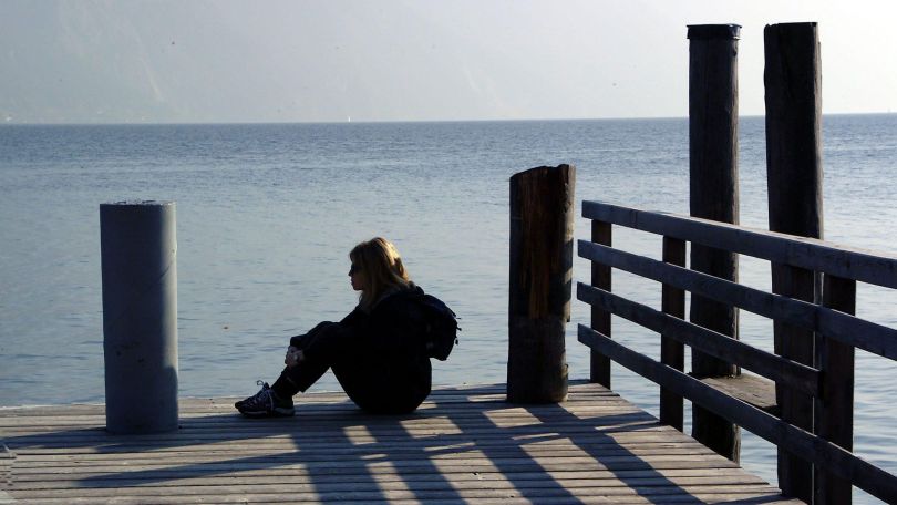 Eine Frau sitz alleine auf einem Steg am Wasser
