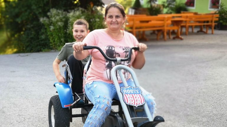 Eine Mutter sitzt vorne am Lenker eines Gokarts, dahinter sitzt ein lachender Bub.