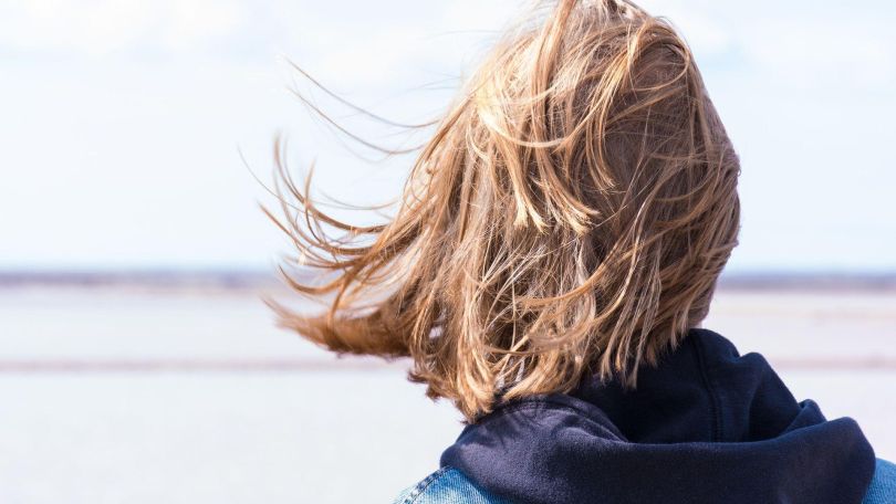 Frau mit brünetten schulterlangen Haaren, schwarzer Kapuzenweste und Jeansjacke blickt in die Ferne