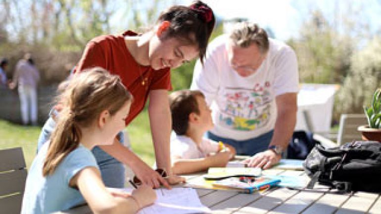 2 Kinder machen Hausaufgaben im Freien und werden von 2 Personen betreut