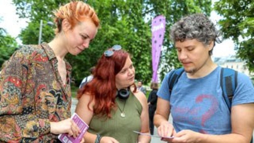 3 Personen in sommerlicher Kleidung stehen vor Bäumen