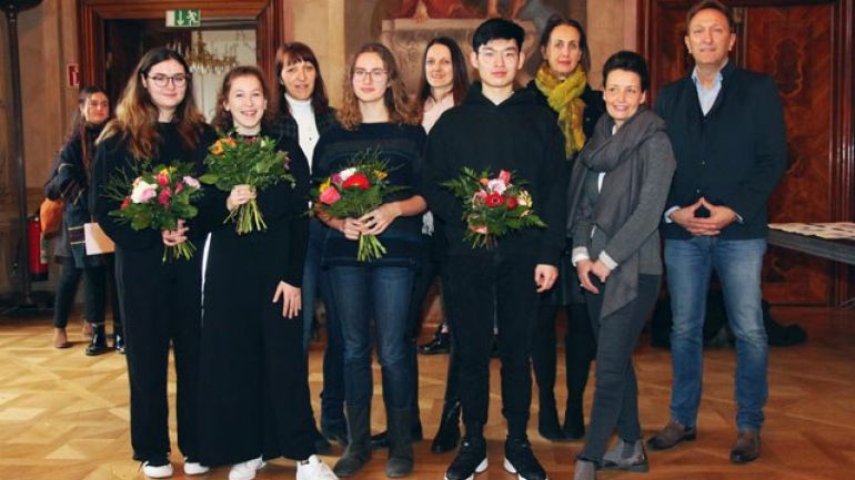 Schülerinnen und Schüler in dunkler Kleidung, 4 davon halten Blumensträuße