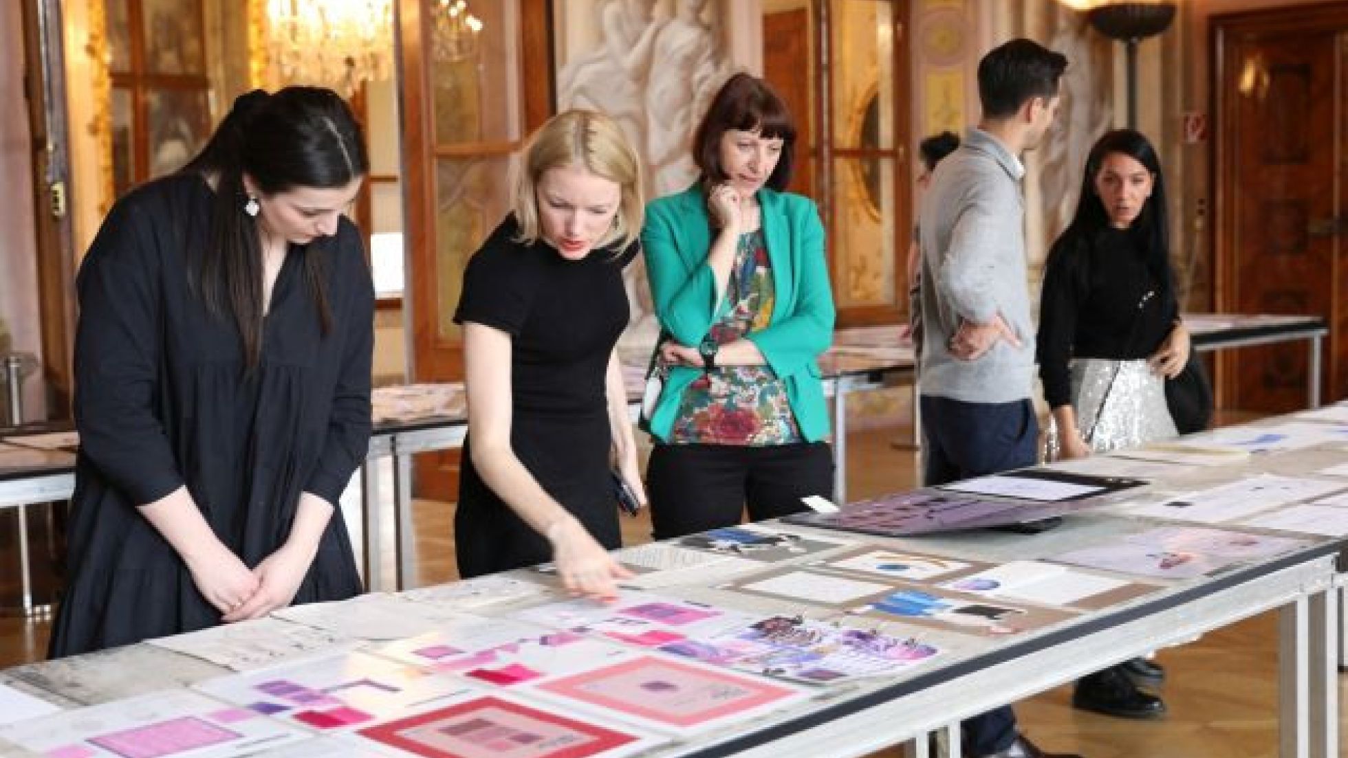 Mehrere Personen betrachten Entwürfe auf einem langen Tisch