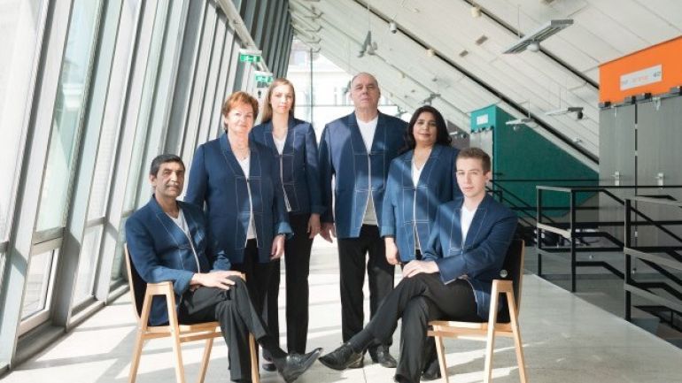 Männer und Frauen mit schwarzen Hosen, weißen Leibchen und blauen Oberteilen im Foyer der Stadthalle