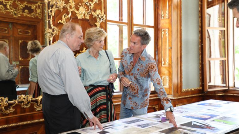 2 Herren zeigen auf eine Ausstellungsfläche, dazwischen eine Dame