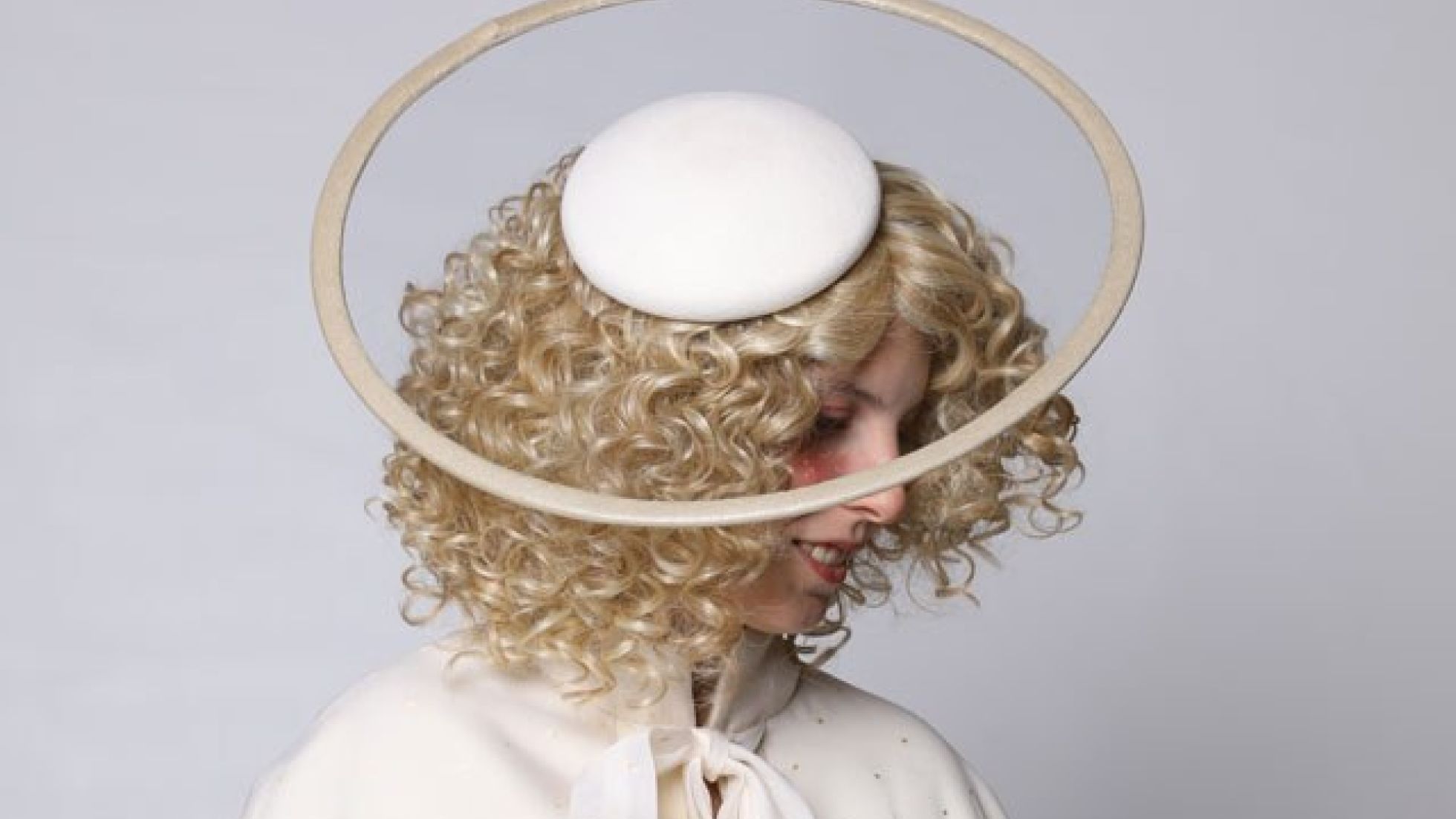 Frau mit goldenen Locken, weißem Umhang und weißem Hut mit Optik eines Heiligenscheins