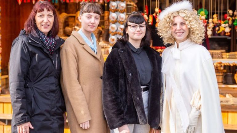 Direktorin, eine Schülerin als Christkind verkleidet sowie zwei Schülerinnen in Wintermänteln vor Adventmarkt-Stand