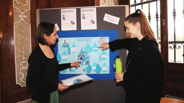 2 Frauen deuten auf ein Plakat auf einer Pinnwand