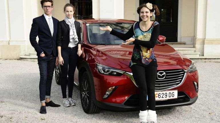 SchülerInnen präsentieren Tuch und Krawatte des Projekts vor Mazda-Wagen