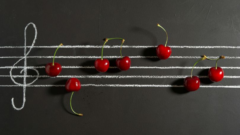 Tafel mit aufgemalter Notenzeile und Notenschlüssel. Auf der Tafel liegen Kirschen, die Noten darstellen sollen.