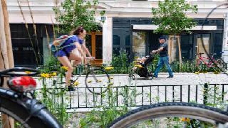 Frau auf Rad, Mann mit Kinderwagen in einer Gasse