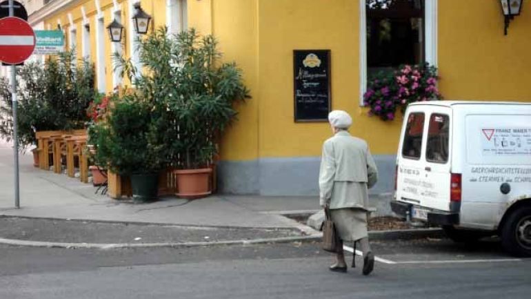 Ältere Dame mit Gehstock überquert eine Straße